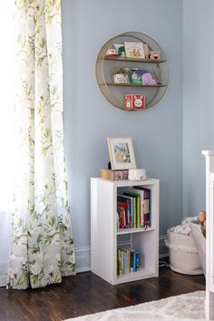 a baby's room with blue walls, white furniture and a book shelf on the wall