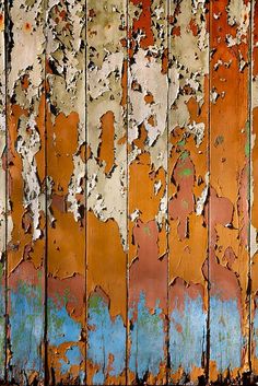 an old rusted wooden wall with blue and orange paint peeling off the wood surface