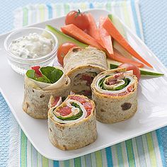 a plate topped with rolls and carrots on top of a blue table cloth next to a bowl of dip