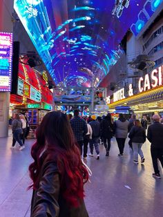 people are walking through an indoor mall with neon lights on the ceiling and signs above them