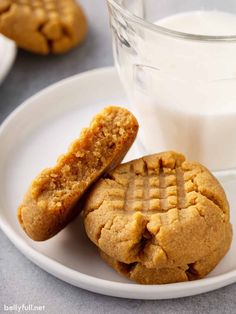 two peanut butter cookies on a white plate next to a glass of milk and some cookies