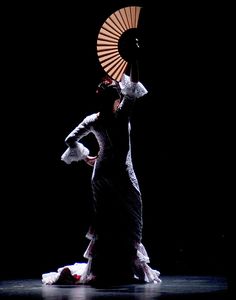 a woman with an umbrella is dancing in the dark, wearing a long black dress