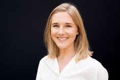 a woman with blonde hair wearing a white shirt and smiling at the camera while standing in front of a black background