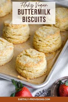 buttermilk biscuits on a baking sheet with strawberries in the background and text overlay