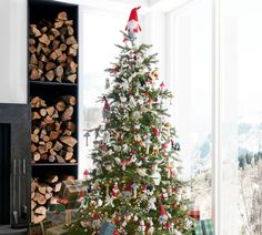 a decorated christmas tree with presents under it in front of a window and firewood stacked on the floor