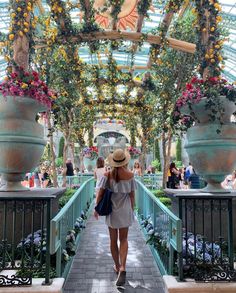 a woman walking down a walkway in a building with lots of flowers hanging from the ceiling