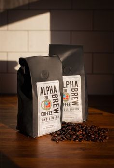 two bags of coffee sitting on top of a wooden table next to some coffee beans