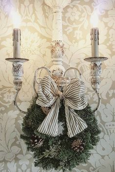 a christmas wreath hanging from the side of a white wall with two candles on it