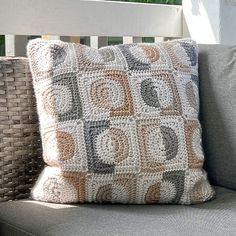 a crocheted pillow sitting on top of a couch next to a wicker chair