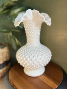 a white vase sitting on top of a wooden table next to a potted plant