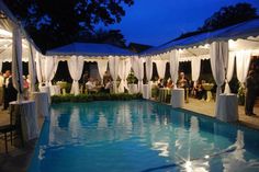 an outdoor pool with white drapes and tables set up for a formal function at night