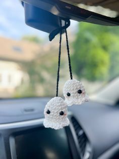 two white sheep hanging from the dash board of a car with black eyes on it