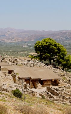 an old building sitting on top of a rocky hill next to a tree and mountains