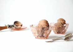 three bowls filled with ice cream next to spoons and utensils on a white surface