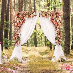 an outdoor wedding ceremony setup with flowers and draping on the trees in the woods