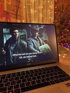 an open laptop computer sitting on top of a table next to a christmas tree with lights