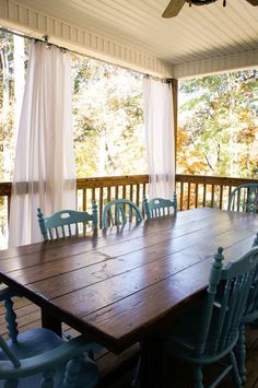 a wooden table with blue chairs on top of it in front of a covered porch