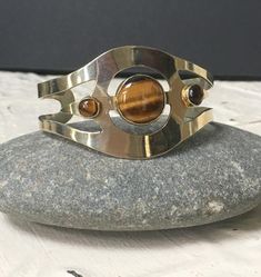 Vintage Silver and Tiger Eye Cuff Bracelet,3 StoneTiger Eye Cuff Bracelet.  Bracelet is cuff style and adjustable.  Measures approximatel 1 3/4" wide at top widest point.  Tiger eye stones are beautiful in color and markings. Largest center stone measures 3/4" in diameter, and 2 smaller stones measure 5/8". I am uncertain of the stamp/marking on this bracelet.  I believe it is stamped "mexico" there are no other markings, so I am uncertain of the purity of the silver.  I was told by a jeweler th Adjustable Modernist Bangle Bracelet, Vintage Bangle Bracelets With Polished Finish, Vintage Bangle Bracelet With Polished Finish, Retro Adjustable Silver Bracelets, Adjustable Retro Silver Bracelet, Retro Adjustable Silver Bracelet, Vintage Adjustable Bracelet With Polished Finish, Retro Silver Bangle Bracelets, Vintage Adjustable Bangle With Polished Finish