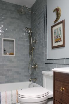 a white toilet sitting next to a bath tub in a bathroom under a framed picture