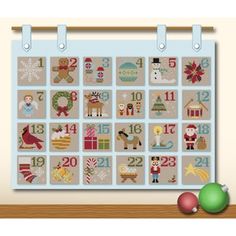 a cross stitch christmas calendar on a wall with ornaments and decorations in front of it