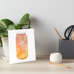 an orange and yellow drink in a mason jar art board on a desk next to a potted plant