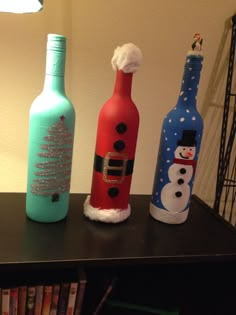 three wine bottles decorated with snowmen and santa hats are sitting on a table in front of a lamp