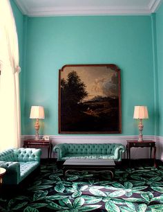 a living room filled with green couches next to two lamps and a painting on the wall