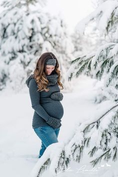 a pregnant woman standing in the snow with her hands on her belly and looking down