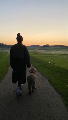 a woman walking her dog down a dirt path at sunset or dawn in the countryside