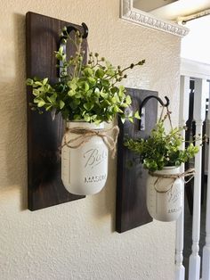 two mason jars are hung on the wall with plants in them and tied to hooks