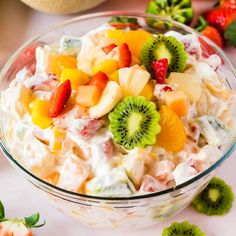 a fruit salad in a glass bowl with strawberries and kiwis on the side