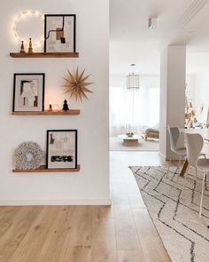 a dining room with white walls and wooden flooring next to a wall mounted shelf filled with pictures