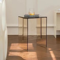 a glass side table with a book on top and a vase in the corner next to it