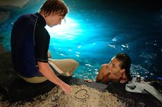 a man and woman sitting next to each other in the water looking at something on the ground