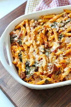 a casserole dish filled with pasta and spinach on a wooden cutting board