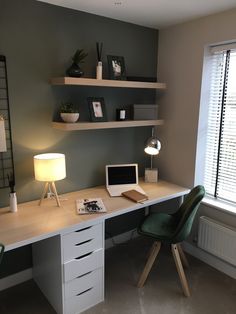 a desk with a laptop, lamp and other items on it in front of a window