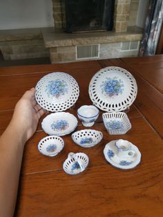 a person is sitting at a table with many plates and cups on it, including one that has blue flowers