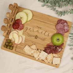 a wooden cutting board topped with apples, grapes and meats next to crackers