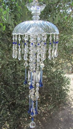 a glass chandelier hanging from the side of a tree in front of some bushes