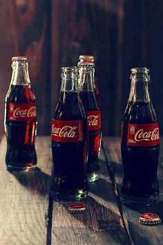 three bottles of coca cola sitting on top of a wooden table