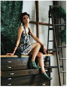 a woman sitting on top of a wooden dresser next to a green plant and ladder