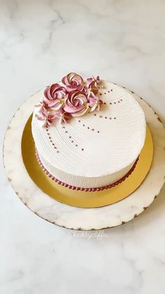 a white cake with pink flowers on top sitting on a marble countertop next to a gold rimmed plate