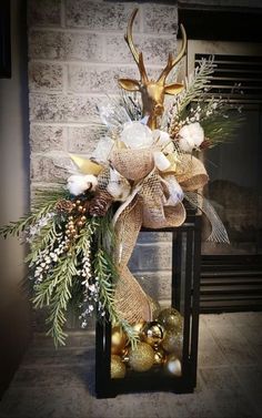 a christmas decoration with gold and white balls, greenery and deer antlers on a fireplace mantel