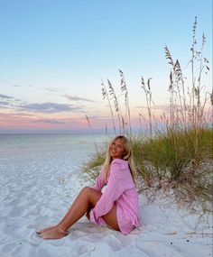 a woman is sitting on the beach with her legs crossed and smiling at the camera