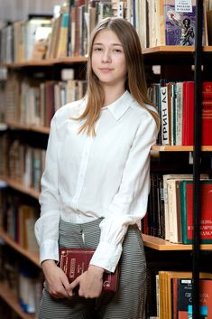 a woman standing in front of a bookshelf holding a red book and looking at the camera