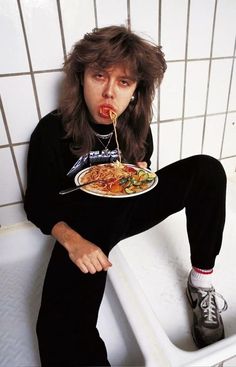 a man sitting in a bathtub with food on his plate and tongue sticking out