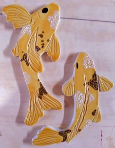 two yellow fish shaped magnets sitting on top of a wooden table next to each other