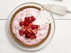 a pie with strawberries on top is sitting on a white table next to utensils