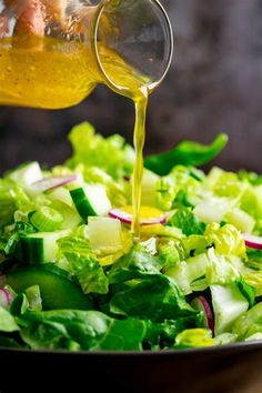 a person pouring dressing into a salad with lettuce and radishes