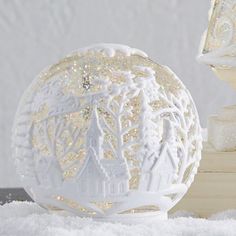 a white snow globe sitting on top of a pile of snow next to a lit candle